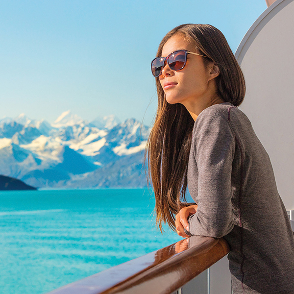 Luxury travel Alaska cruise holiday woman relaxing on balcony looking at view of mountains and nature landscape. Asian girl sunglasses tourist.; Shutterstock ID 1115696984; purchase_order: AAA Vacations 2022; job: ; client: ; other: 