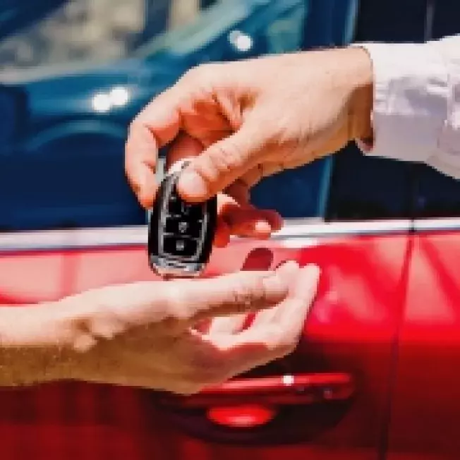 Hand handing over keys to another hand with red car in background