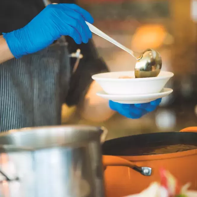 Person ladeling soup into a bowl in a restaurant kitchen