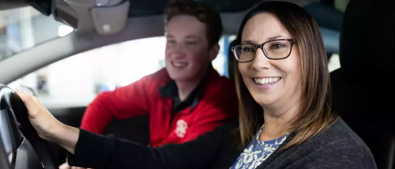 woman in the drivers seat wearing glassess smiling out the window with a CAA representative in a red shirt smiling in the passenger seat