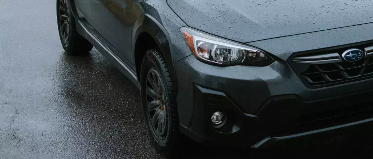 Close up image of the front right of a dark green subaru with rain pellets