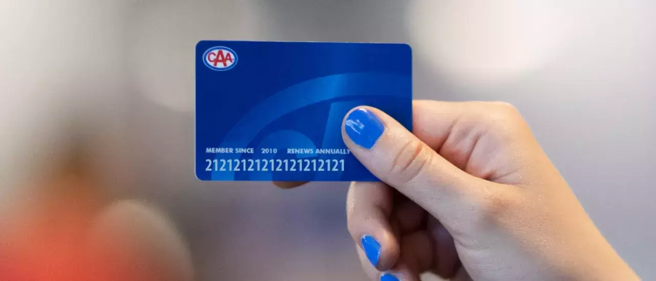 hand with blue nailpolish holding a blue CAA membership card with the CAA logo at the top left 