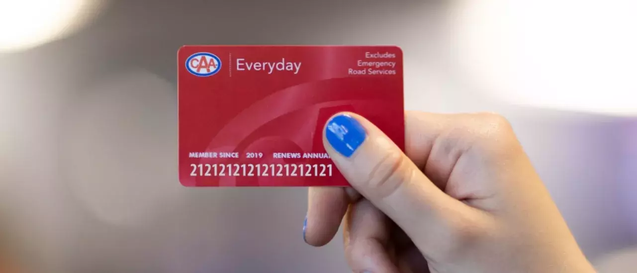 hand with blue nailpolish holding a red CAA membership card with the word Everyday at the top left to the right of the CAA logo. Top right of the card says Excludes Emergency Road Services