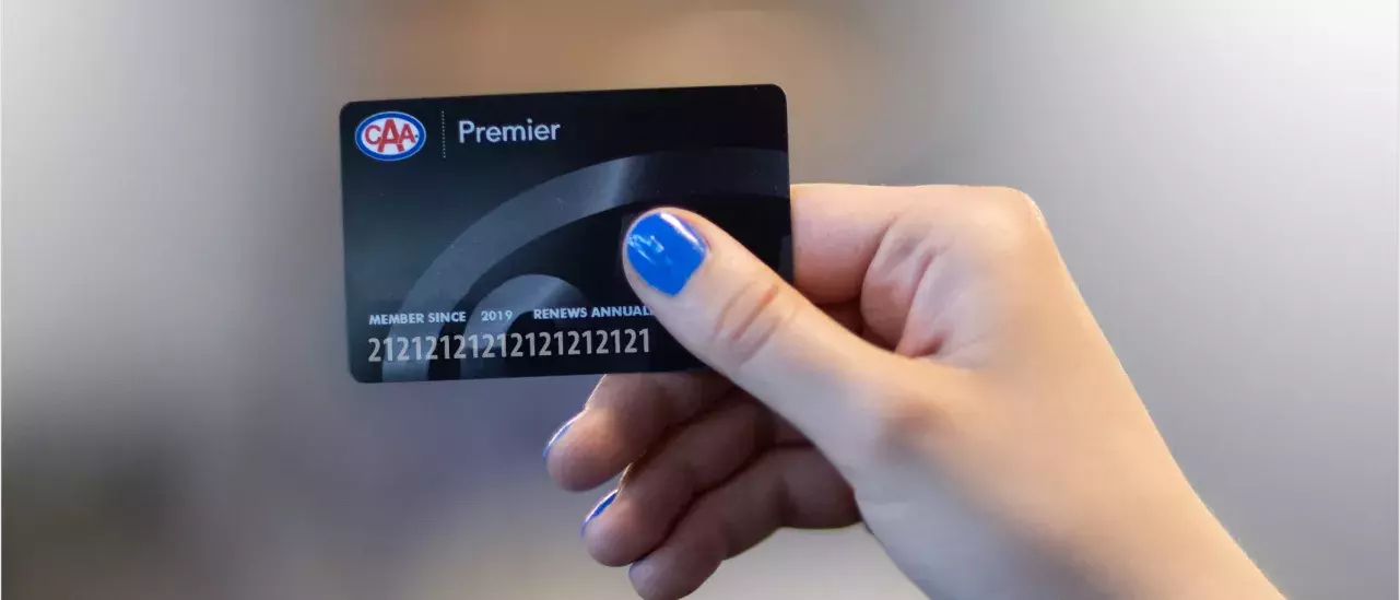 hand with blue nailpolish holding a black CAA membership card with the word Premier listed at the top to the right of a CAA logo