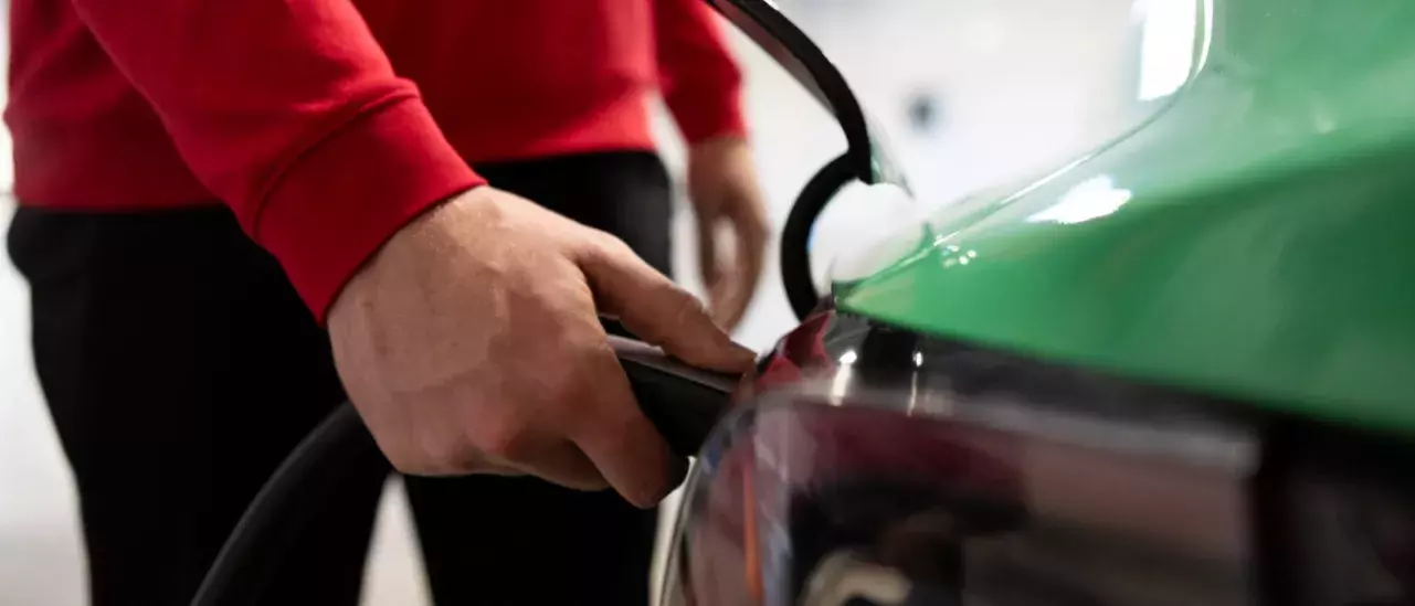 Close up of a hand holding an electric vehicle charger to a car