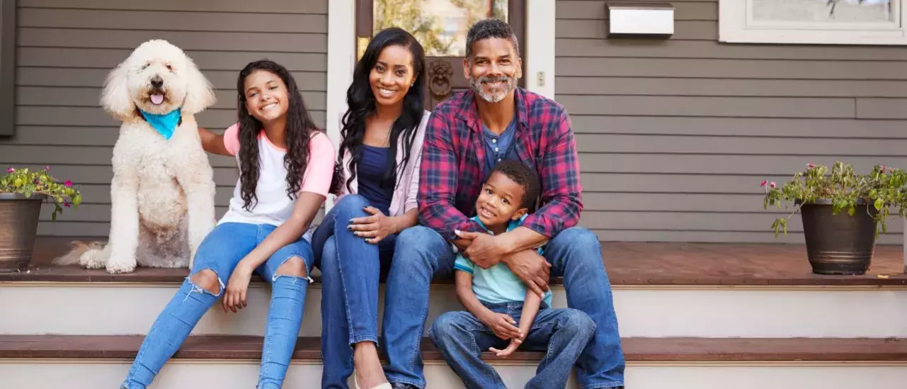 Family of four sits on the front step of their house with their white dog. 