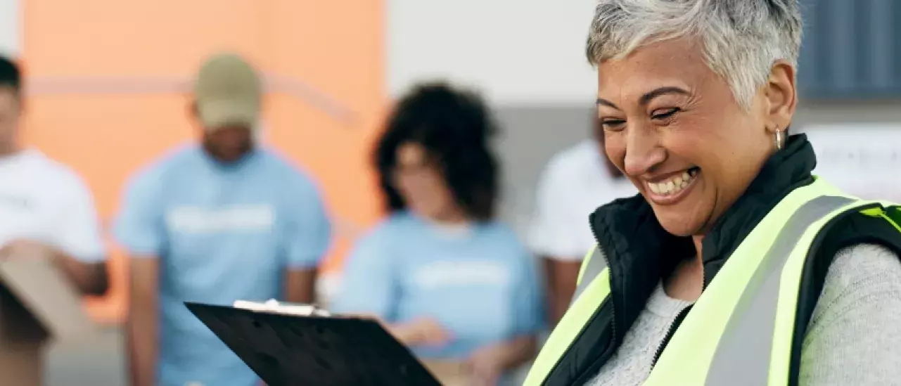 Woman in a neon vest smiling holding a clipboard with three people in the background