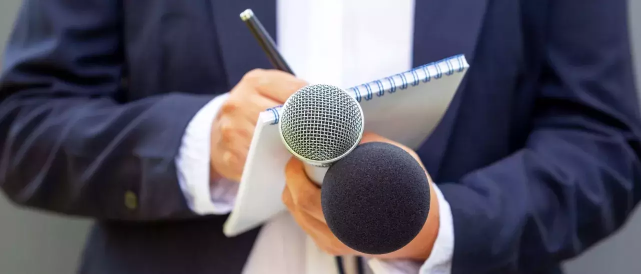 Close up shot of a man in a suit holding a pad, paper and a microphone