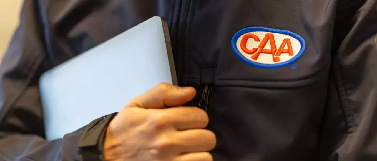 CAA agent wearing a branded CAA jacket, holding a laptop