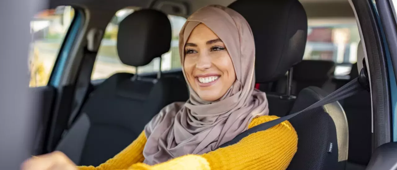 Woman wearing a hijab smiling in the drivers seat of a car