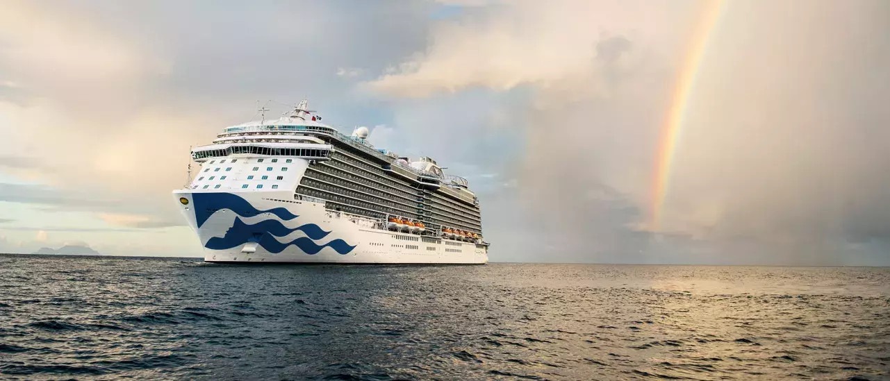 A cruise ship sailing at sea with a rainbow in the background