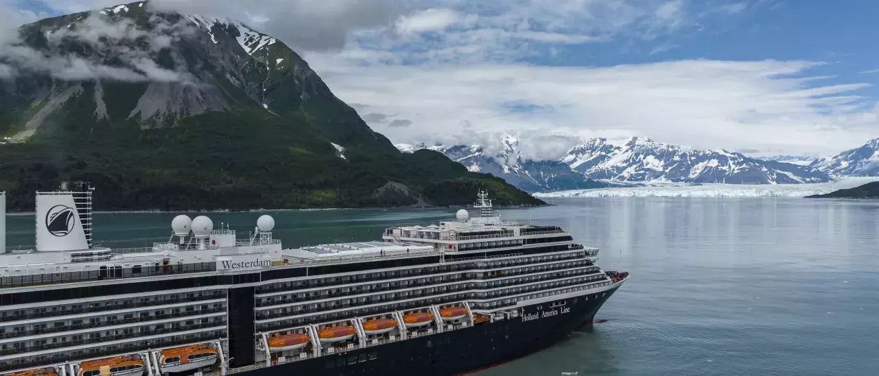 A Holland America Line cruise ship sails past mountains and glaciers.