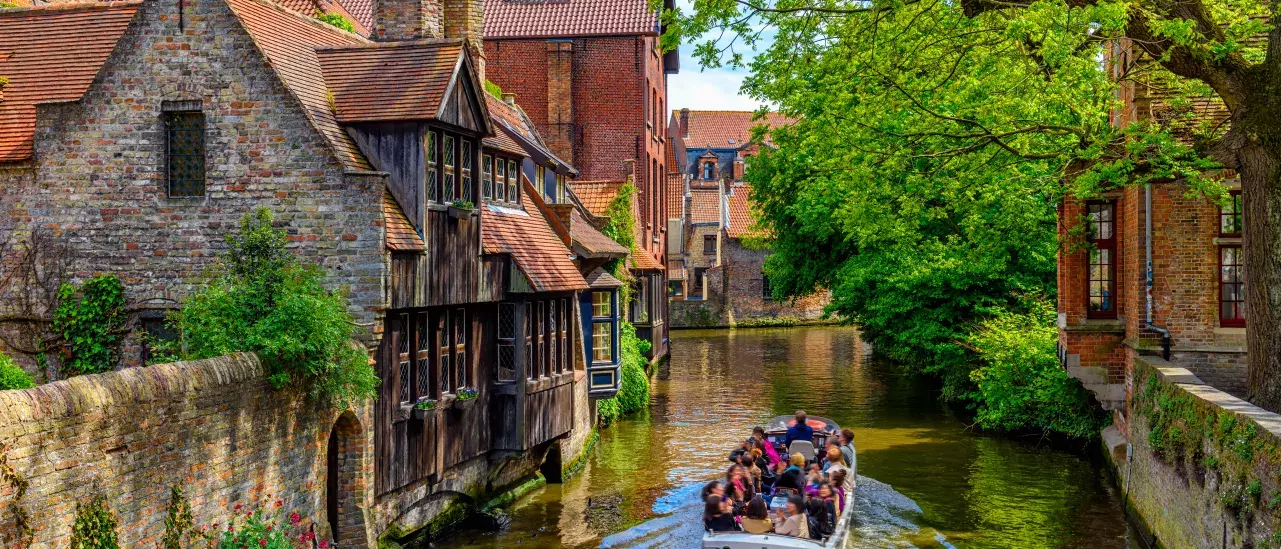 Tour boat on a canal in Bruges, Belgium, surrounded by historic buildings and greenery.