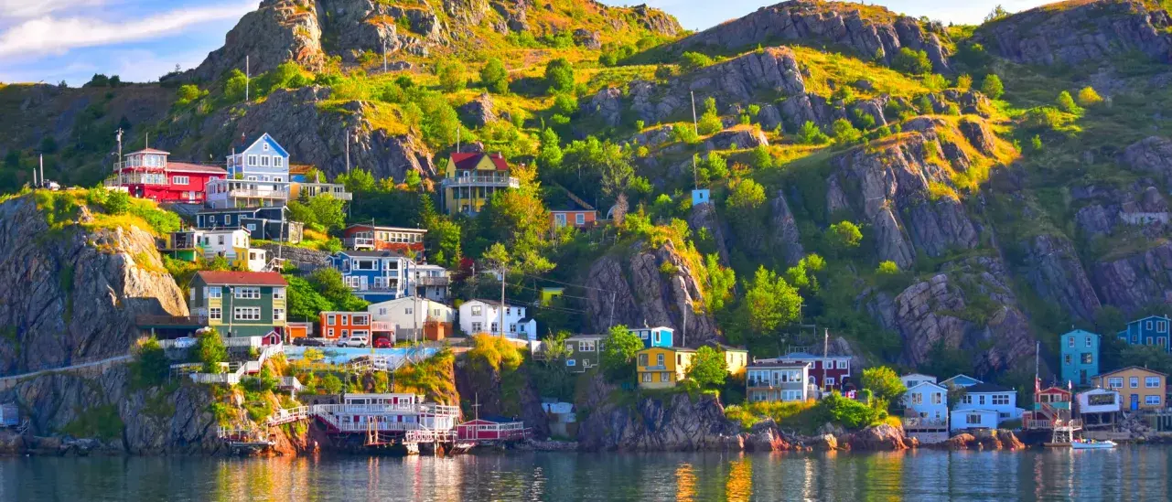 A coastal village with colorful houses built on a rocky hillside, reflecting in the calm water below.
