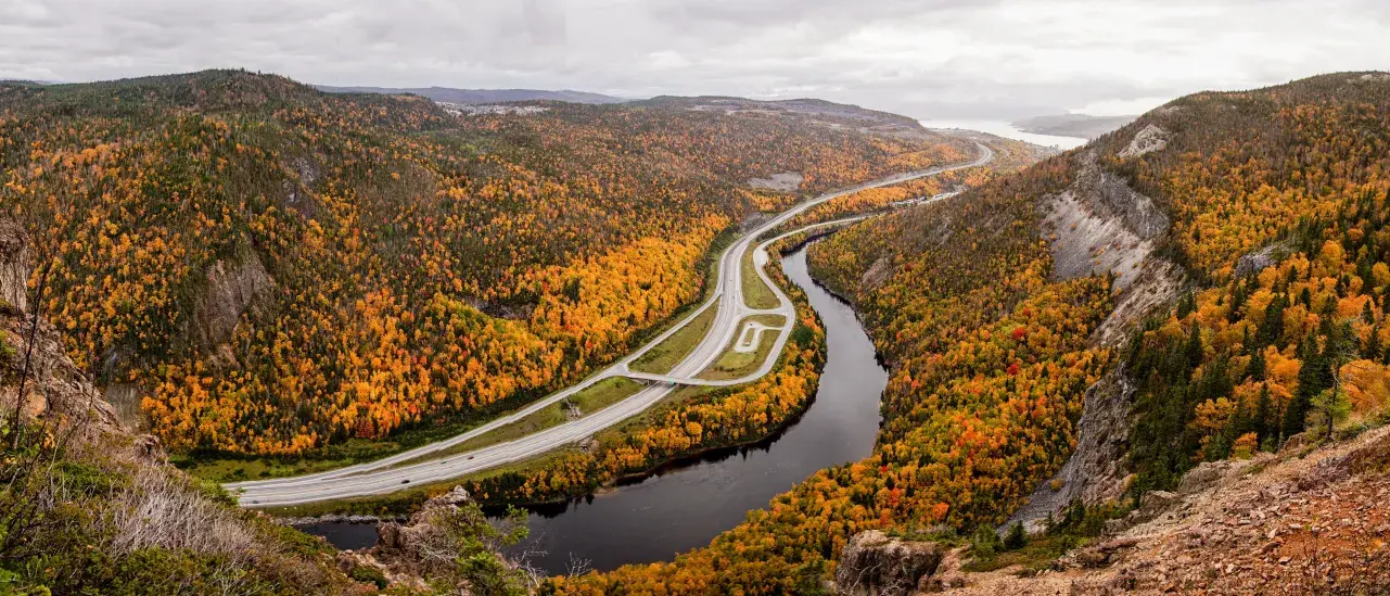 Winding highway through a colorful autumn valley with a river and forested hills.