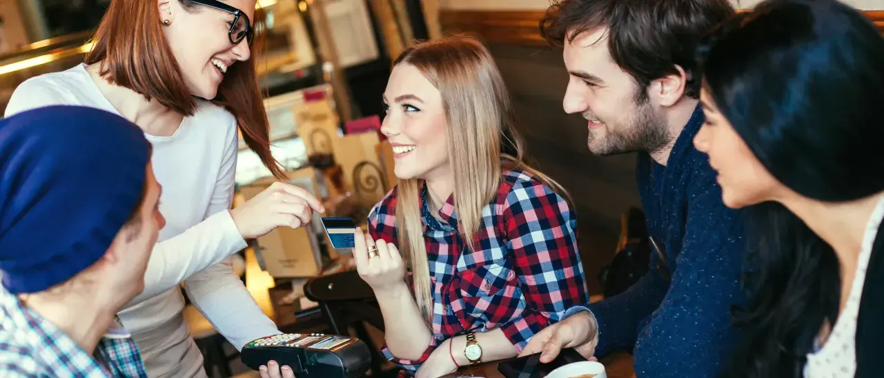 Group at café table paying with credit card, server smiling.
