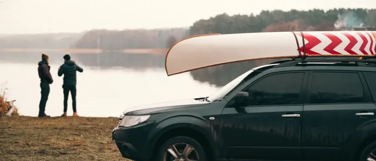 SUV parked by a lake with a canoe on the roof, two people standing by the water in the background.