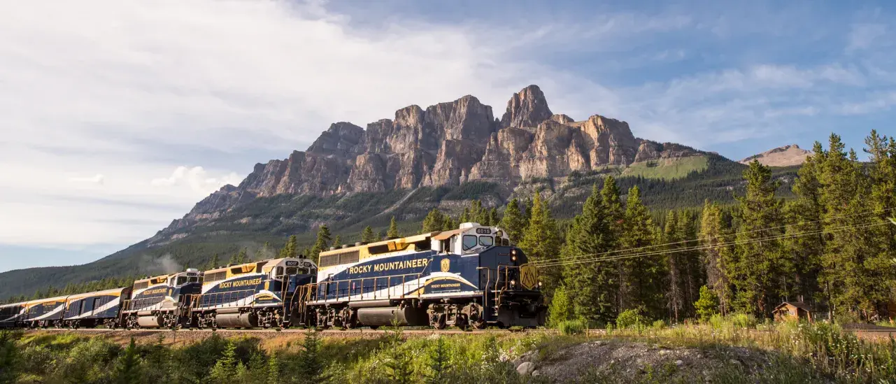 Rocky Mountaineer train travelling through the Canadian Rockies with Castle Mountain in the background.