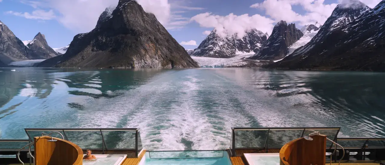 Cruise ship hot tubs overlooking turquoise water and snow-covered mountains with a glacier.