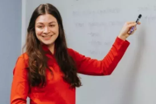 Woman in a red shirt holding a marker to a whiteboard