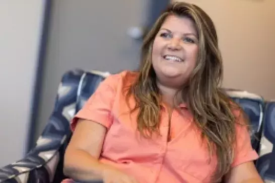 woman wearing an orange short sleeve collard shirt smiling in an armchair