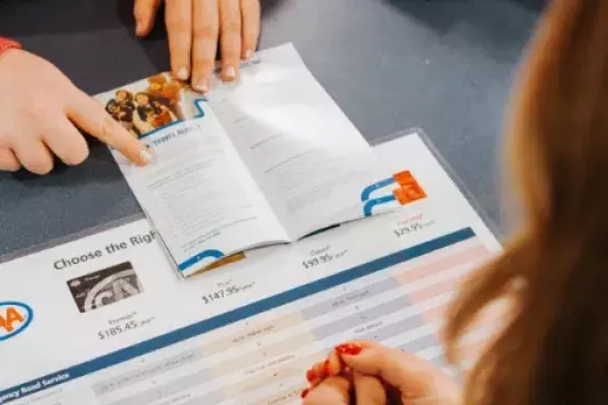 Person pointing to a pamphlet on a table on top of a chart outlining membership plans