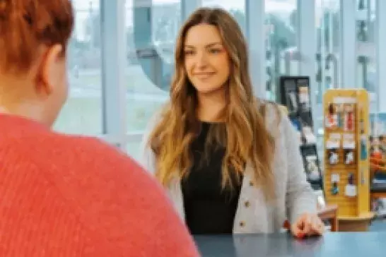 female with long brown hair wearing a grey cardigan being asissted by a representative at a counter