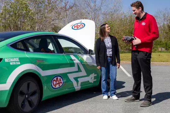 A woman standing next to a CAA worker holding onto an EV charger. Both standing next to a EV with the hood up