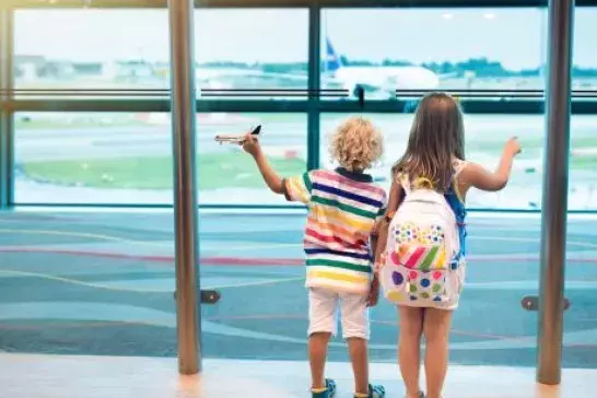 Two children standing with the backs to the camera watching planes land at the airport