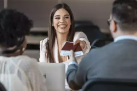 A male and female couple talking to a CAA agent who is handing them back their passports smiling 