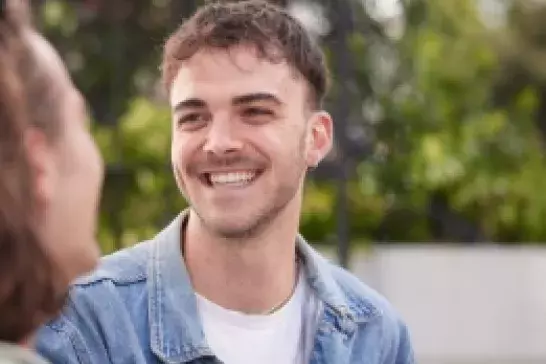 young man wearing a jean jacket and white tshirt smiling at the person he is sitting next to