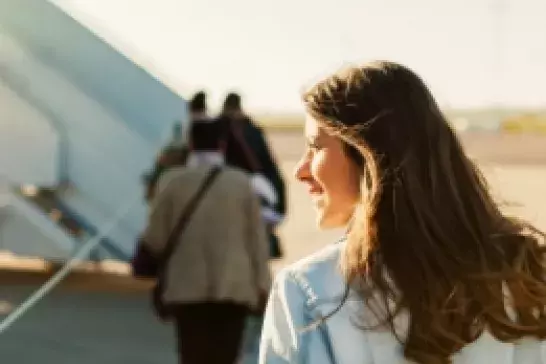 Woman walking across tarmac approaching a boarding stair to plane