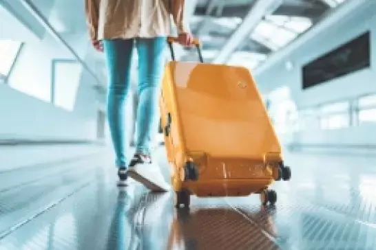 Person walking through airport with yellow luggage