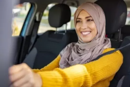 Woman wearing a hijab smiling in the drivers seat of a car