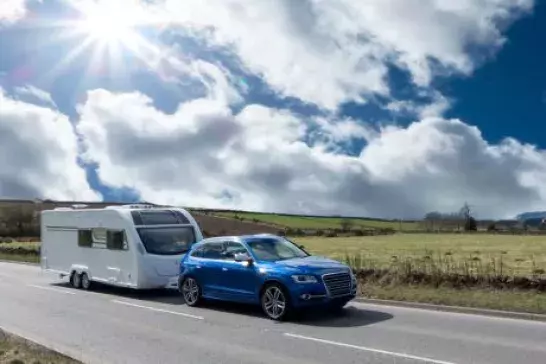 Blue SVU towing a family camer down the highway, surrounded by grassy fields on a sunny day. 