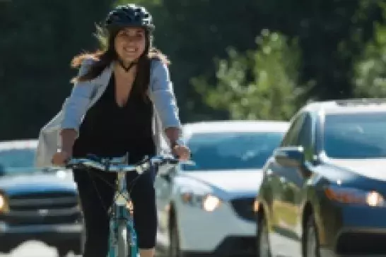 Woman on a bike wearing a helmut cycling next to cars