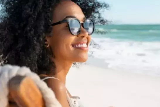 a young afriacn-american woman smiling wearing sunglasses sitting in a beach chair with the ocean in the background