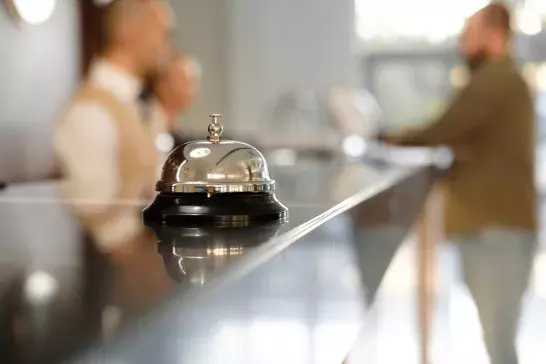 Modern luxury Hotel Reception Counter desk with Bell. Service Bell locating at reception. Silver Call Bell on table, Receptionists and customer on background. Сheck in hotel. 