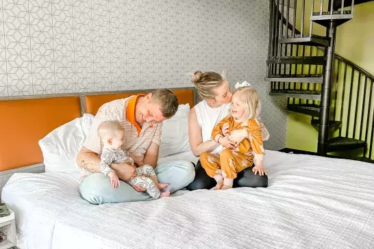 Family sitting on bed in hotel room looking happy and relaxed