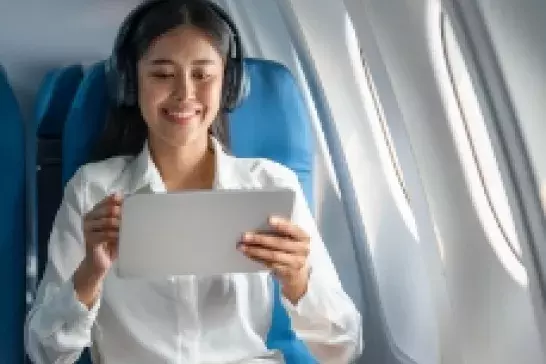 Woman on an iPad sitting on an airplane with headphones on in a window seat