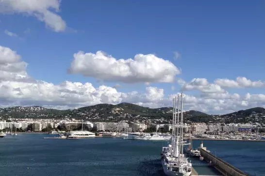 The image shows a scenic coastal view of a marina with a large sailboat docked near a pier.