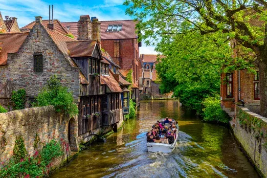 Tour boat on a canal in Bruges, Belgium, surrounded by historic buildings and greenery.