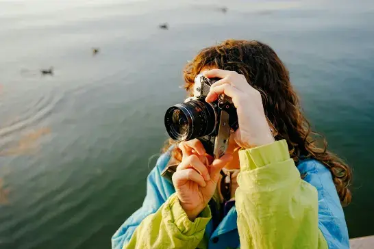 A woman outdoors taking a photograph with her camera.