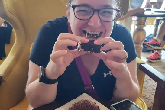 Tanya sitting indoors at a table eating a dessert and smiling.