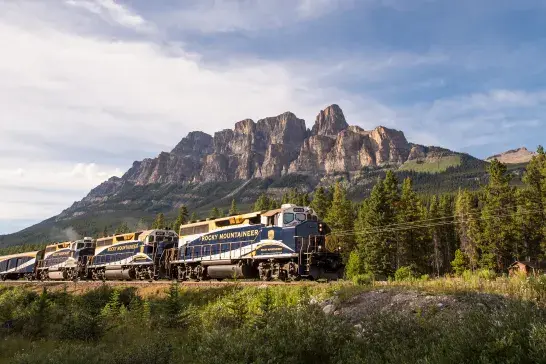 Rocky Mountaineer train travelling through the Canadian Rockies with Castle Mountain in the background.