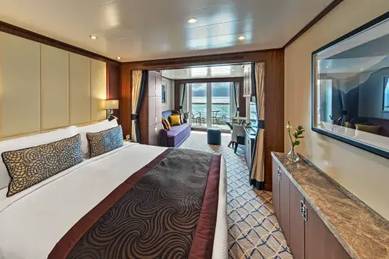 A spacious room on the cruise ship with a bed, seating area, and a balcony.