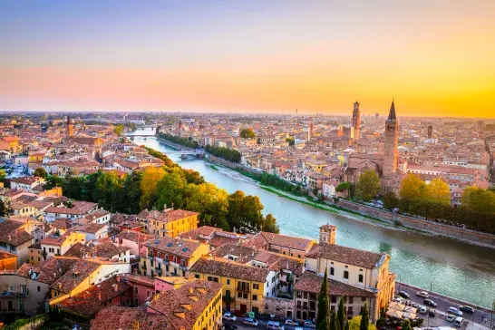 Aerial sunset view of Verona, Italy, with the Adige River, historic buildings, bridges, and church towers stretching across the cityscape.