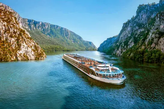 AmaWaterways river cruise ship cruising through a picturesque European river valley surrounded by dramatic cliffs and lush greenery.