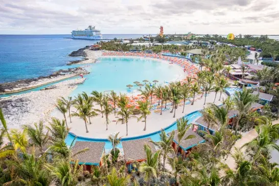 Aerial view of a private island beach resort featuring turquoise lagoon waters, palm trees and a cruise ship offshore.