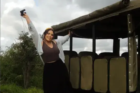 Cass Royea posing beside an open-air safari vehicle on a cloudy day in a wildlife reserve.